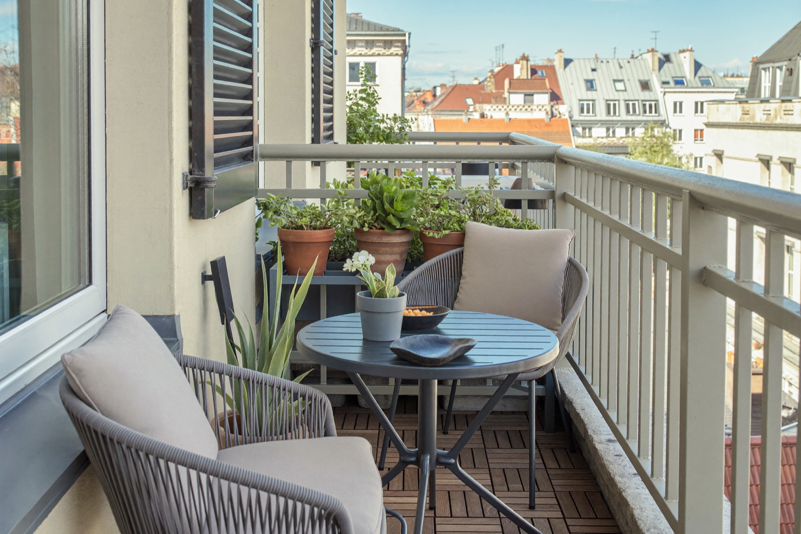 Mały balkon z aluminiowym stolikiem, dwoma krzesłami z technorattanu i roślinami w donicach w słoneczny dzień