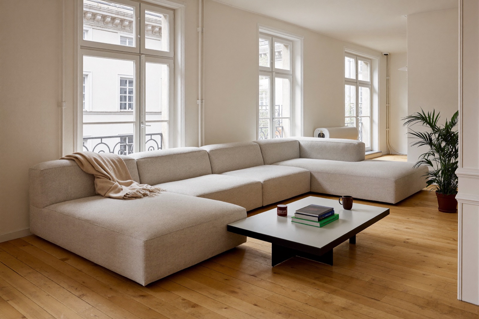 Jasna sofa modułowa w słonecznym salonie z drewnianą podłogą i dużym oknem